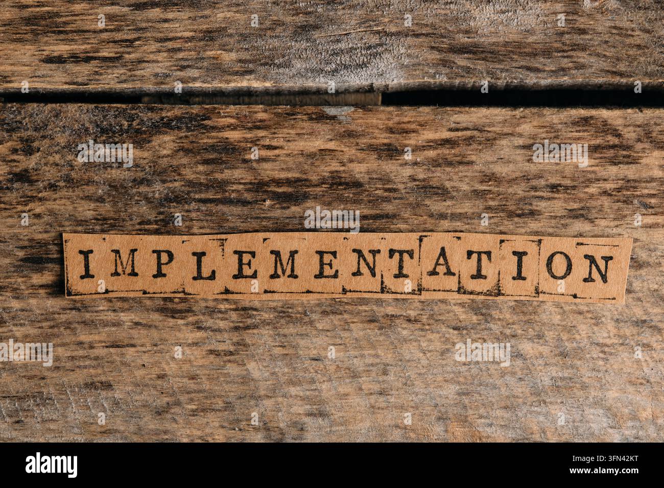 Striscia di carta con la parola "implementazione" stampata con lettere da timbro su una texture di legno rustico Foto Stock
