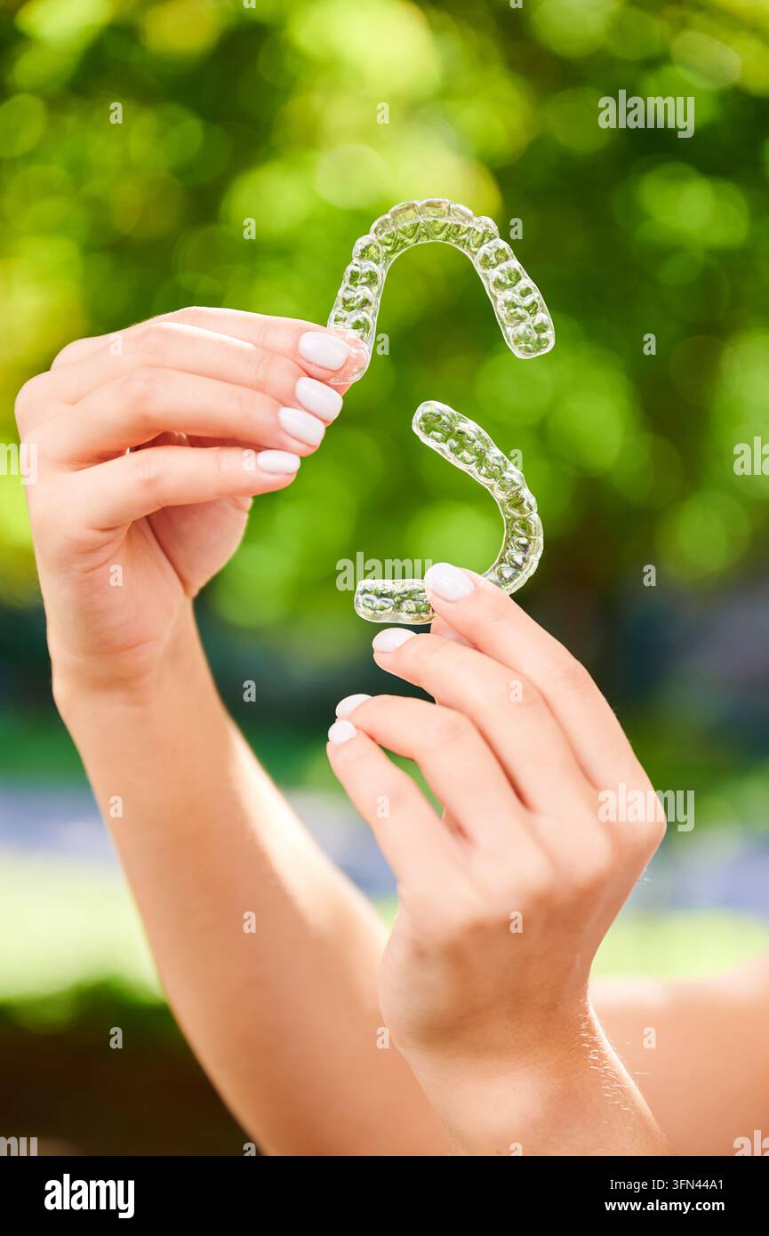 Foto ravvicinata di protezioni dentali per la bocca. Giovane donna che tiene protezioni trasparenti su sfondo verde. Concetto di cura dentale sui denti. Foto Stock