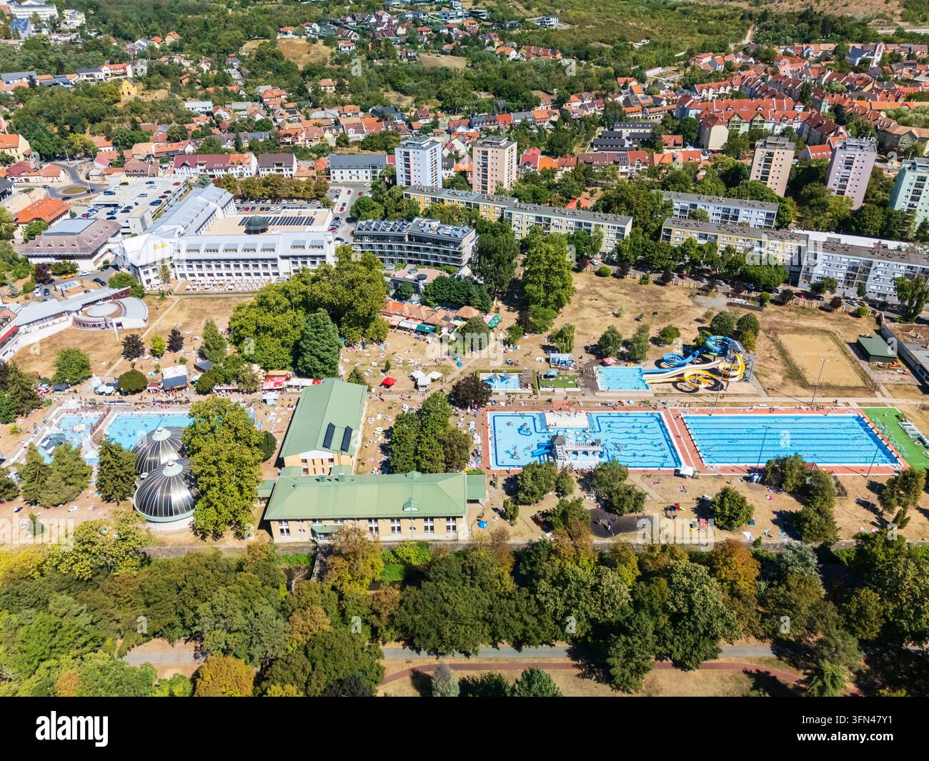 Vista aerea di piscine termali all'aperto affollate, scivoli d'acqua e edifici termali accanto ai quartieri urbani frondosi di Eger, in Ungheria, durante il tempo libero estivo Foto Stock