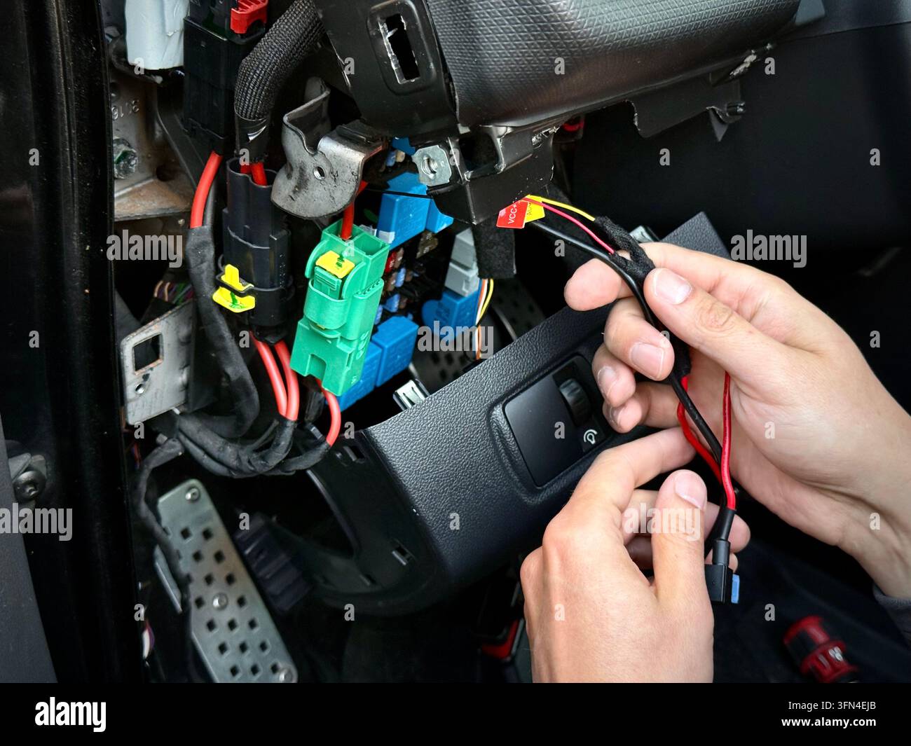 Primo piano delle mani di un tecnico che tiene il cablaggio elettrico vicino al quadro dei fusibili esposto e al cruscotto all'interno dell'abitacolo di una Renault Clio RS. - Immagine stock catturata con smartphone