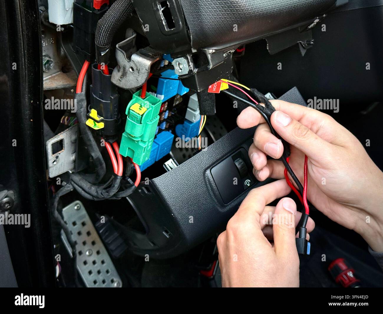 Primo piano delle mani di un tecnico che tiene il cablaggio elettrico vicino al quadro dei fusibili esposto e al cruscotto all'interno dell'abitacolo di una Renault Clio RS. - Immagine stock catturata con smartphone