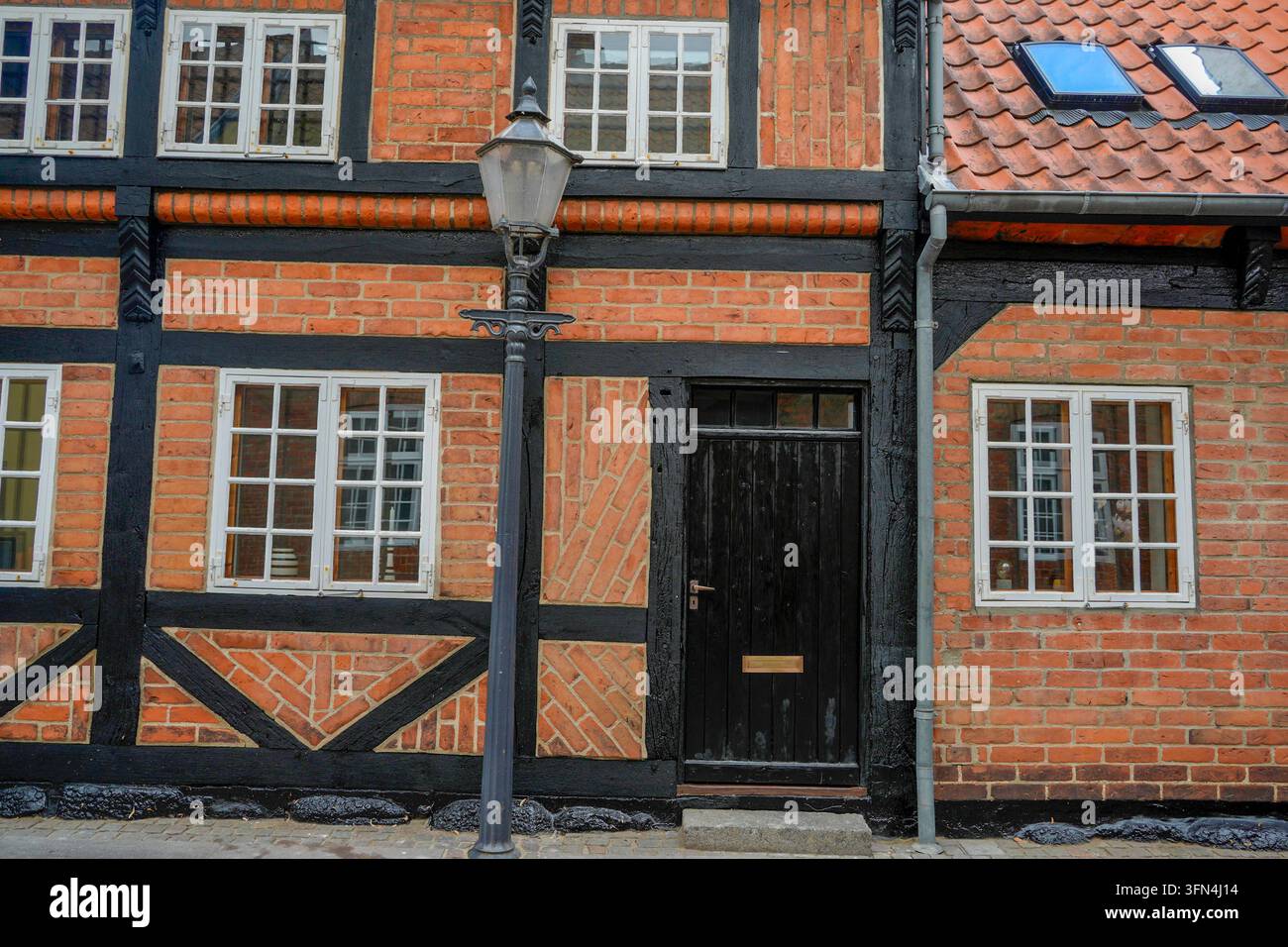 Edificio tradizionale danese a graticcio con riempimento in mattoni rossi, travi in legno nero, finestre incorniciate di bianco e un lampione vintage a Ribe. Foto Stock