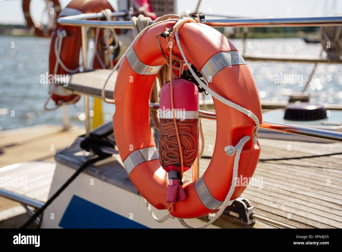 Anello di salvataggio arancione con nastro riflettente montato sulla ringhiera di una barca a vela, simboleggiante sicurezza marina, salvataggio e viaggi marittimi Foto Stock