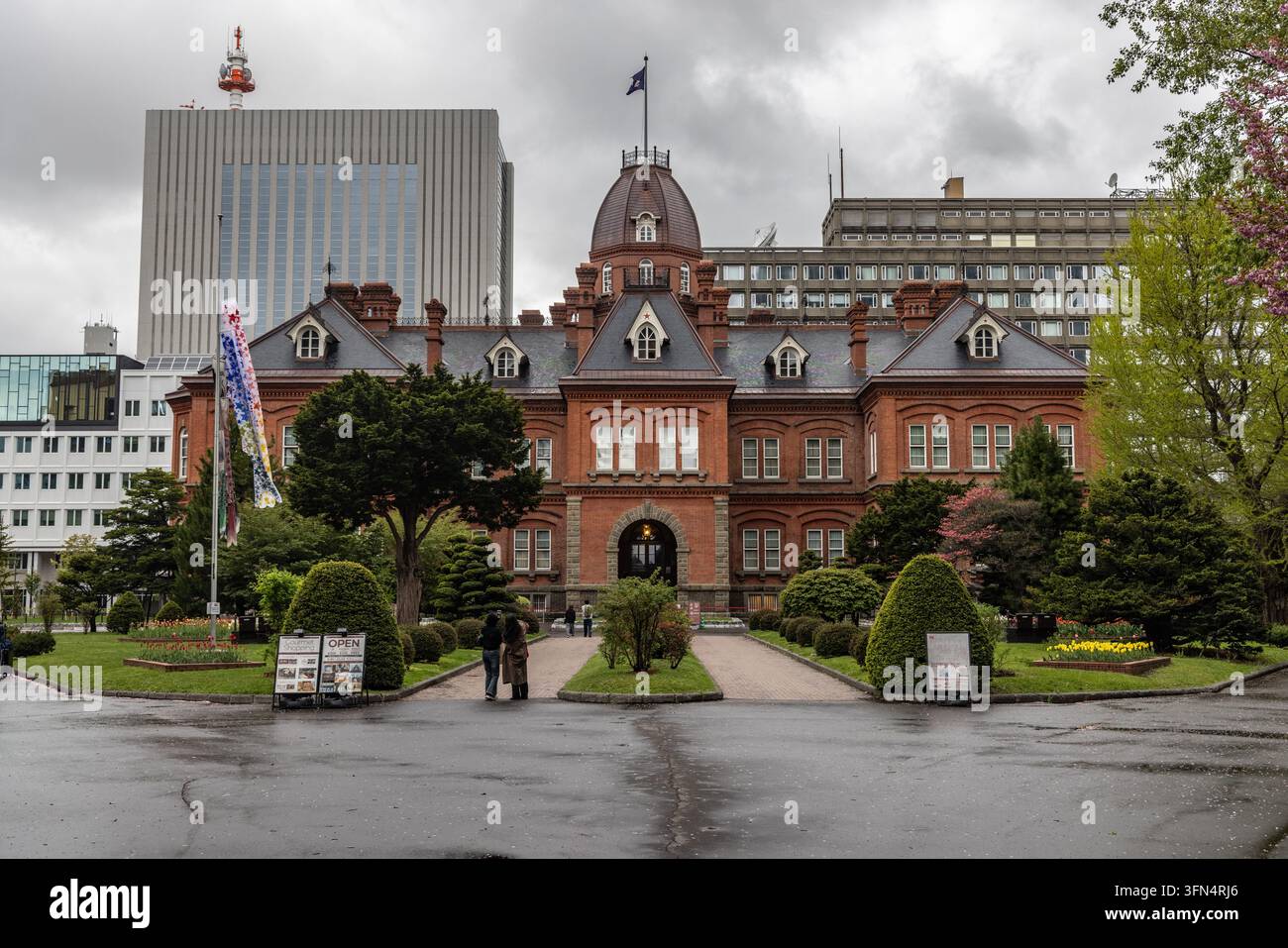 Vista dell'ex edificio governativo storico di Hokkaido con la sua distintiva facciata in mattoni rossi e cupola centrale, circondato da giardini rigogliosi e moderna c Foto Stock