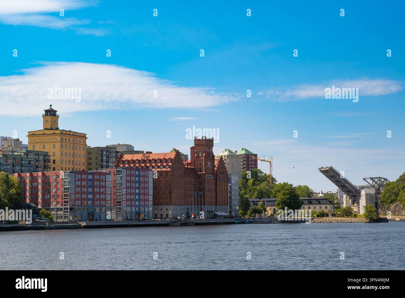 Vista grandangolare dell'edificio storico del mulino di Saltsjoqvarn in mattoni rossi, della torre gialla simbolo, degli appartamenti moderni sul lungofiume e del ponte basculante Danviksbron Foto Stock