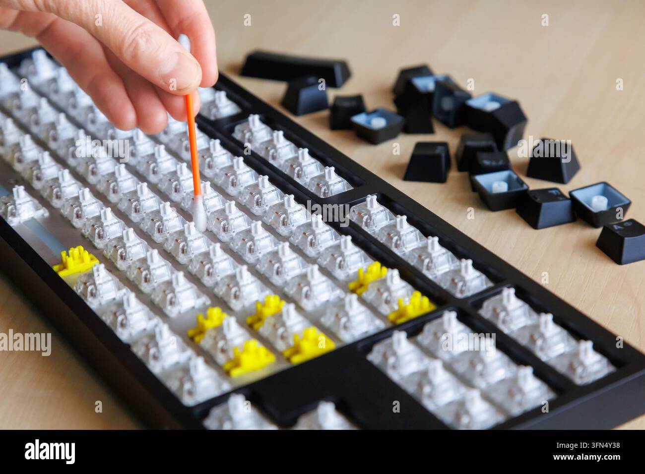 Mano che pulisce gli interruttori esposti della tastiera con una piccola spazzola, tasti rimossi, manutenzione della tastiera fai-da-te, rimozione della polvere, cura dell'hardware del computer. Foto Stock