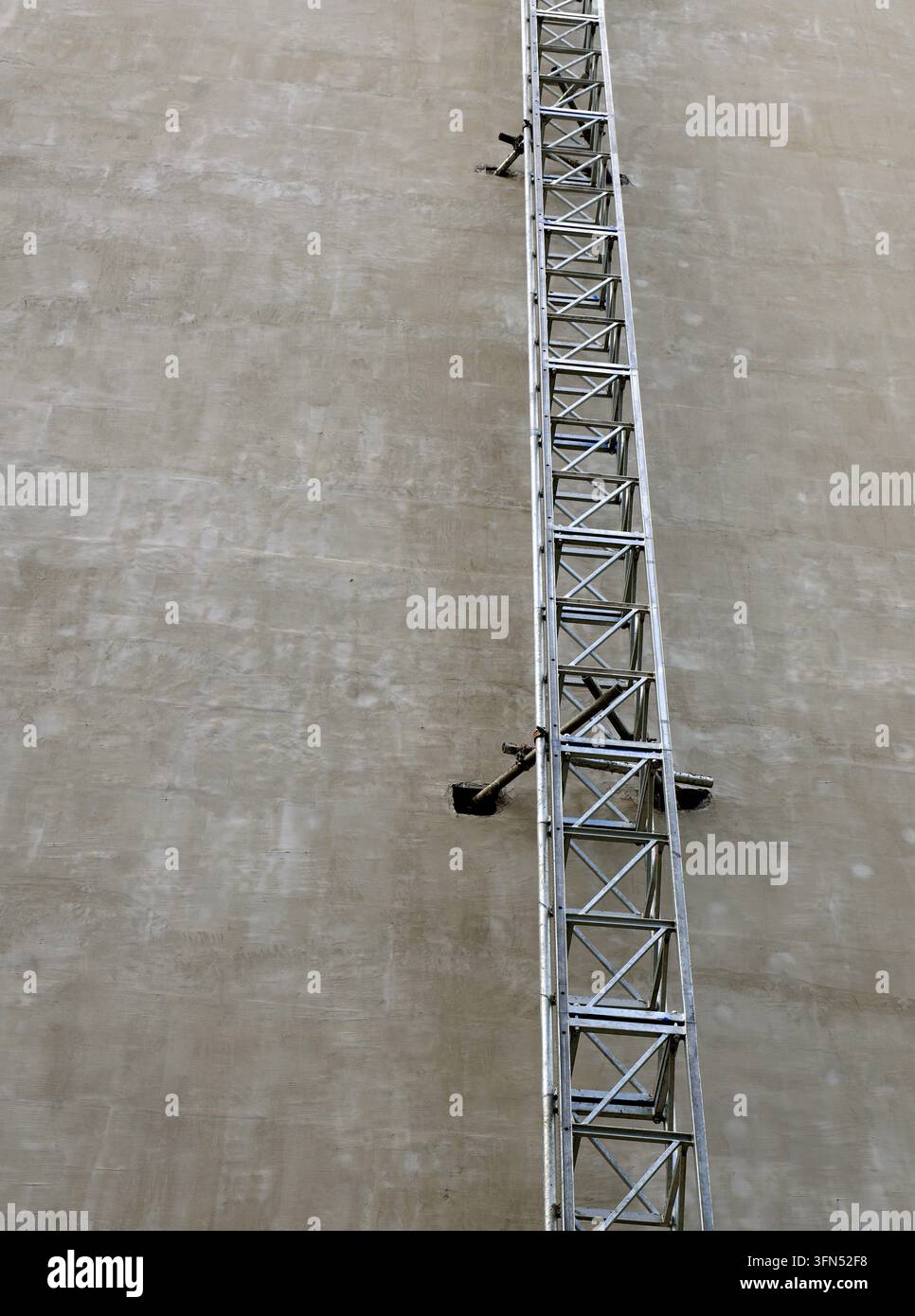 Struttura a scala metallica con elementi di ponteggio fissati verticalmente contro un muro di cemento ruvido, evidenziando il progresso costruttivo e l'industria Foto Stock