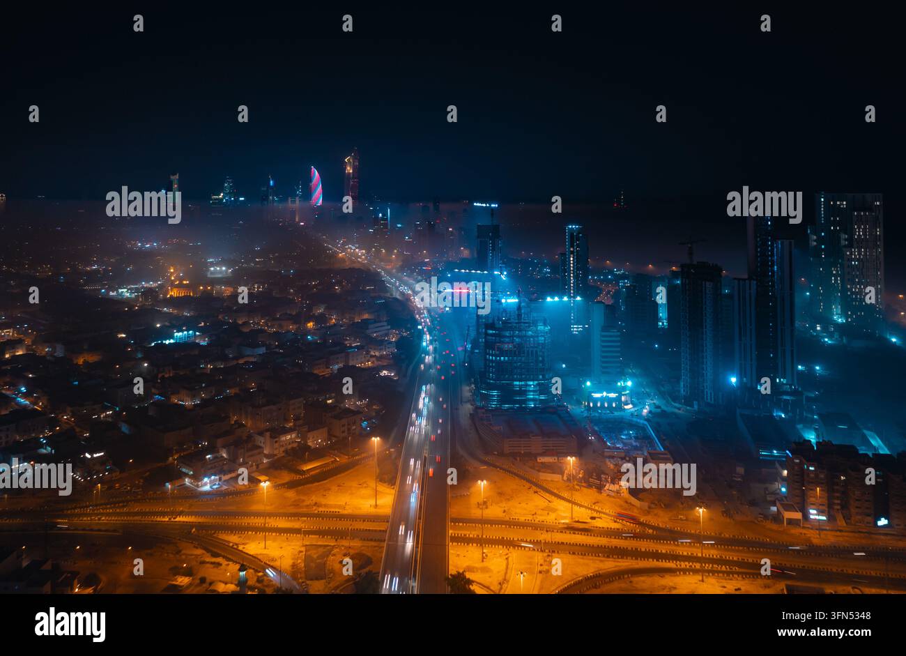 Veduta aerea di uno snodo autostradale, scie di semafori e torri illuminati di blu nella nebbia di notte, Kuwait City, Kuwait Foto Stock