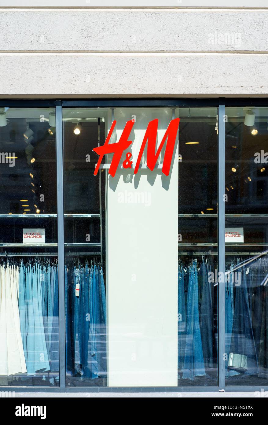 Leoben, Austria - 22.04.2026 Le vetrine di HM mostrano abiti e jeans dietro finestre di vetro. Concetto di moda, vendita al dettaglio, shopping, commercio, stile Foto Stock