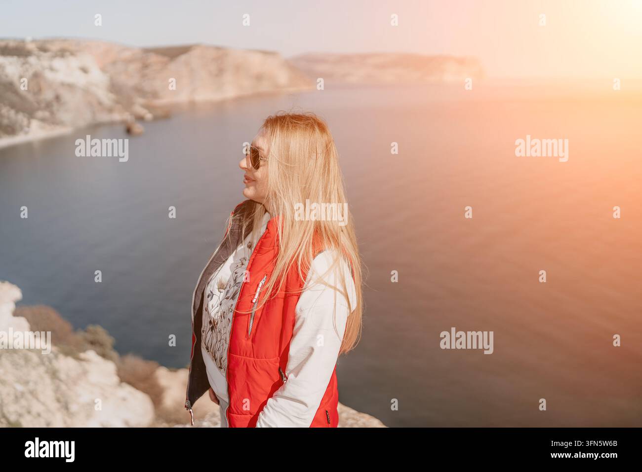 Donna su una scogliera costiera in piedi su un bordo roccioso che si affaccia su una baia scenografica al tramonto mentre godersi un momento di viaggio rilassante Foto Stock