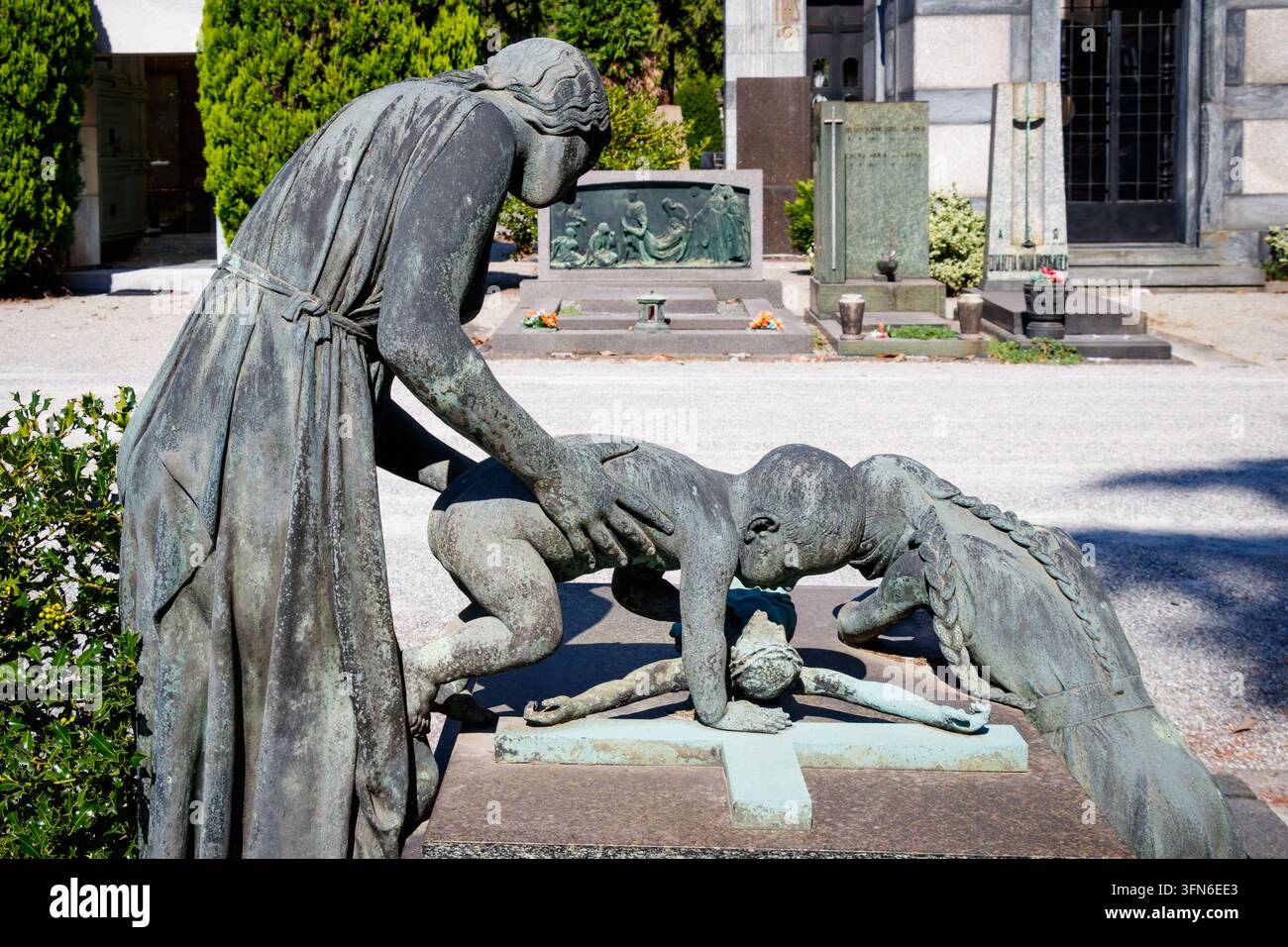 Scultura funebre in bronzo con donna e bambini intorno a una croce sulla tomba Cimitero Monumentale di Milano Cimitero Monumentale di Milano Italia Foto Stock