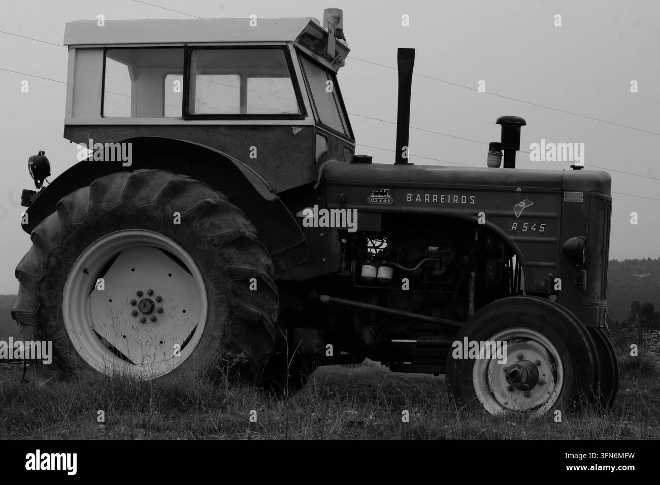 Vista laterale di un trattore vintage Barreiros R 545 parcheggiato in un campo, catturato in bianco e nero evidenziando il suo design classico e la grande utilità agricola Foto Stock