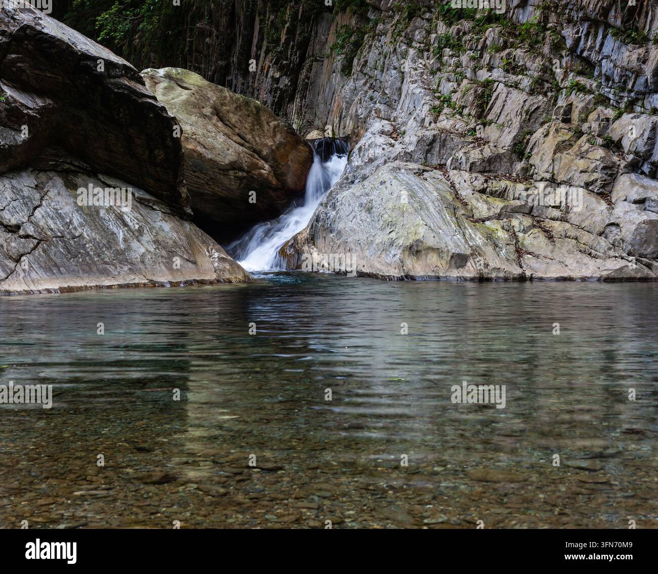 Fiume Sanzhanxi a Hualien, Taiwan. Una piccola cascata sfocia in una chiara piscina naturale. Formazioni rocciose impervie circondano il ruscello. Foto Stock