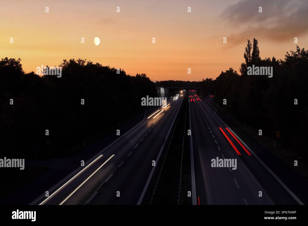 Esposizione lunga del traffico su un'autostrada al tramonto con la luna nel cielo Foto Stock