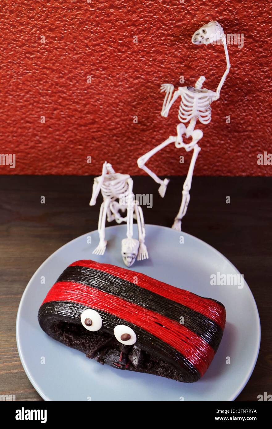 Pastry al cioccolato spaventoso decorato con mini giocattoli a forma di scheletro per uno spuntino a tema Halloween Foto Stock