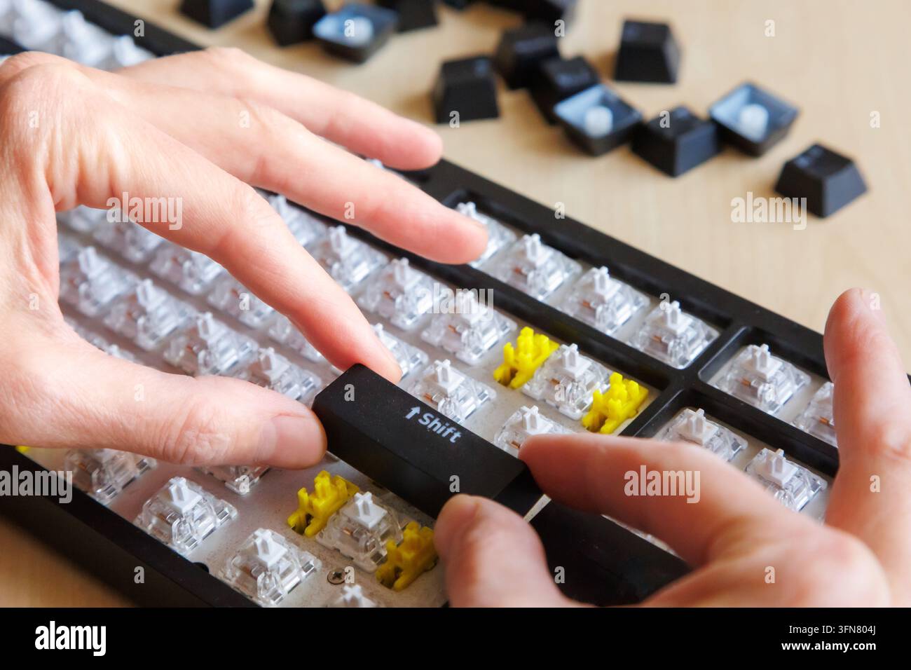 Mani che reinstallano il tasto Maiusc su una tastiera di computer smontata, riassemblaggio dopo la pulizia, riparazione hardware fai-da-te, manutenzione della tastiera, cura del computer. Foto Stock