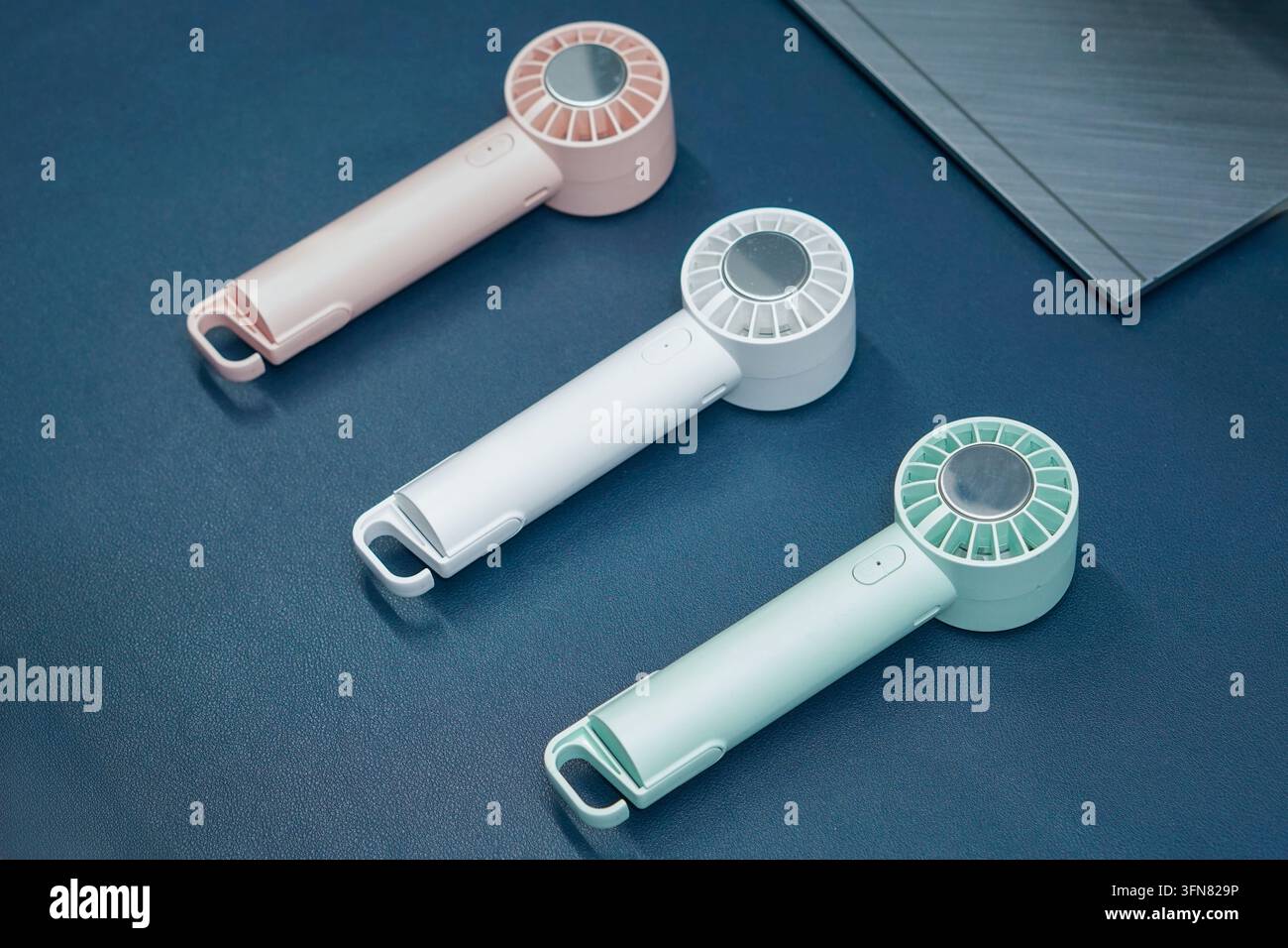 Tre ventole elettriche portatili moderne in colori pastello morbidi posate su una superficie da scrivania blu scuro. Foto Stock
