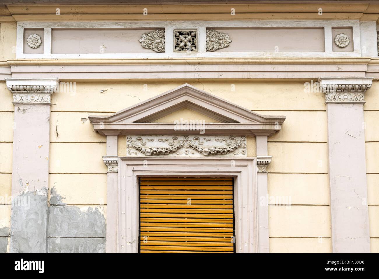 Una vista dettagliata della facciata di un vecchio edificio con una finestra classica con persiane gialle e intagli ornamentali, Sremski Karlovci, Vojvodina, Serbia Foto Stock
