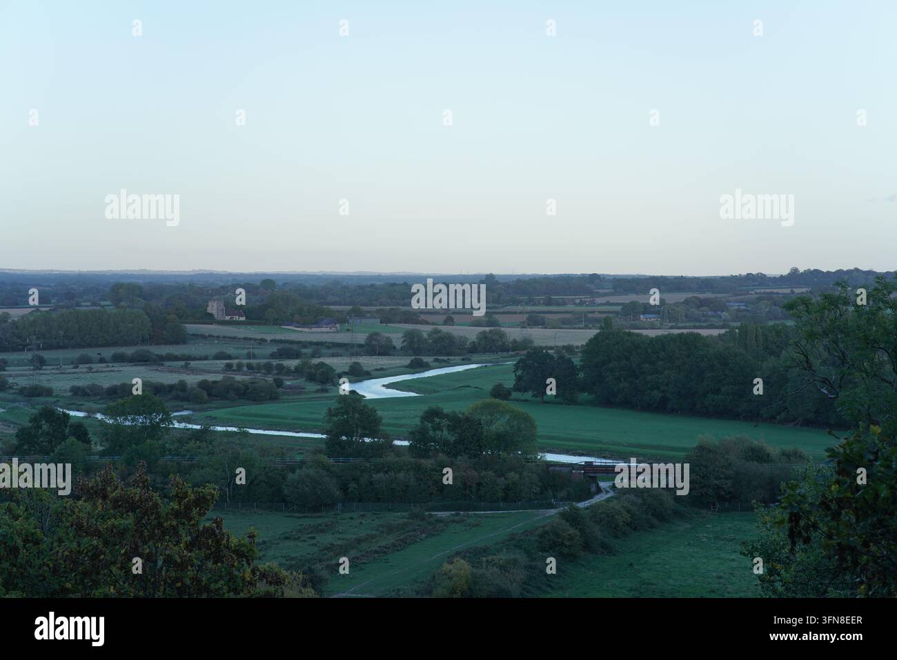 Il fiume Ouse si snoda attraverso i campi verdi della valle vicino a Lewes. Gli alberi incorniciano la vista, con i South Downs all'orizzonte. Foto Stock