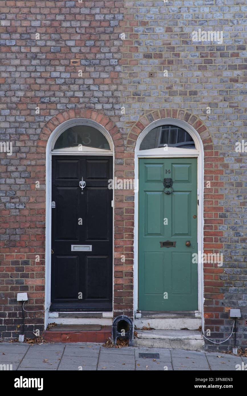 Una porta nera si trova accanto a una porta verde numerata 55 a Lewes. Entrambe hanno abbaini e batacchioni, inseriti in archi di mattoni sopra i gradini. Foto Stock