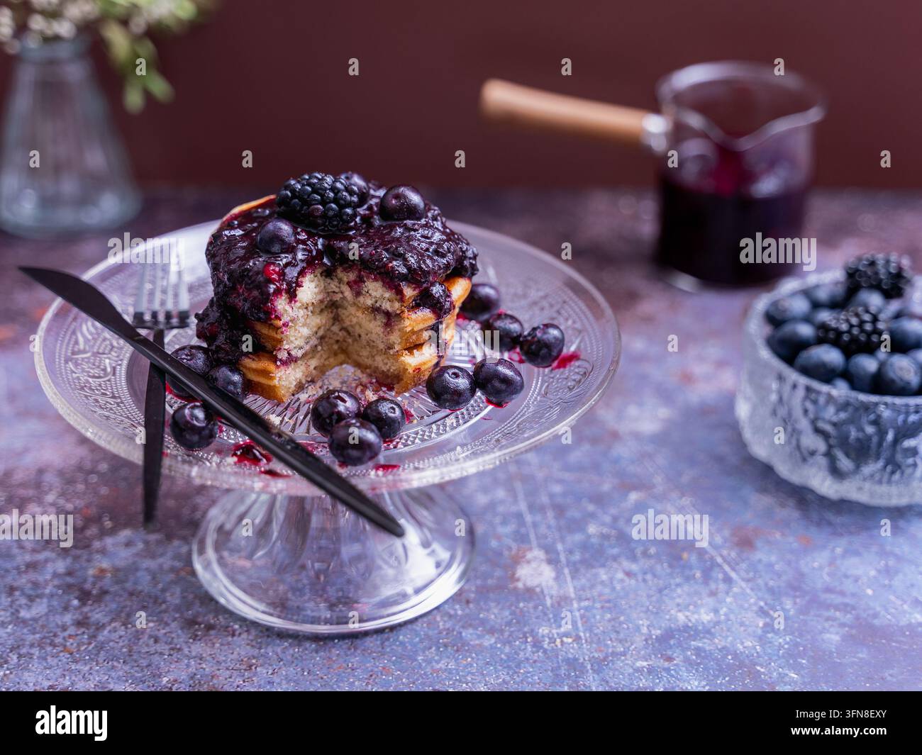 Prima vista di pancake soffici con composta di bacche e bacche fresche serviti su un elegante supporto per torte in vetro Foto Stock