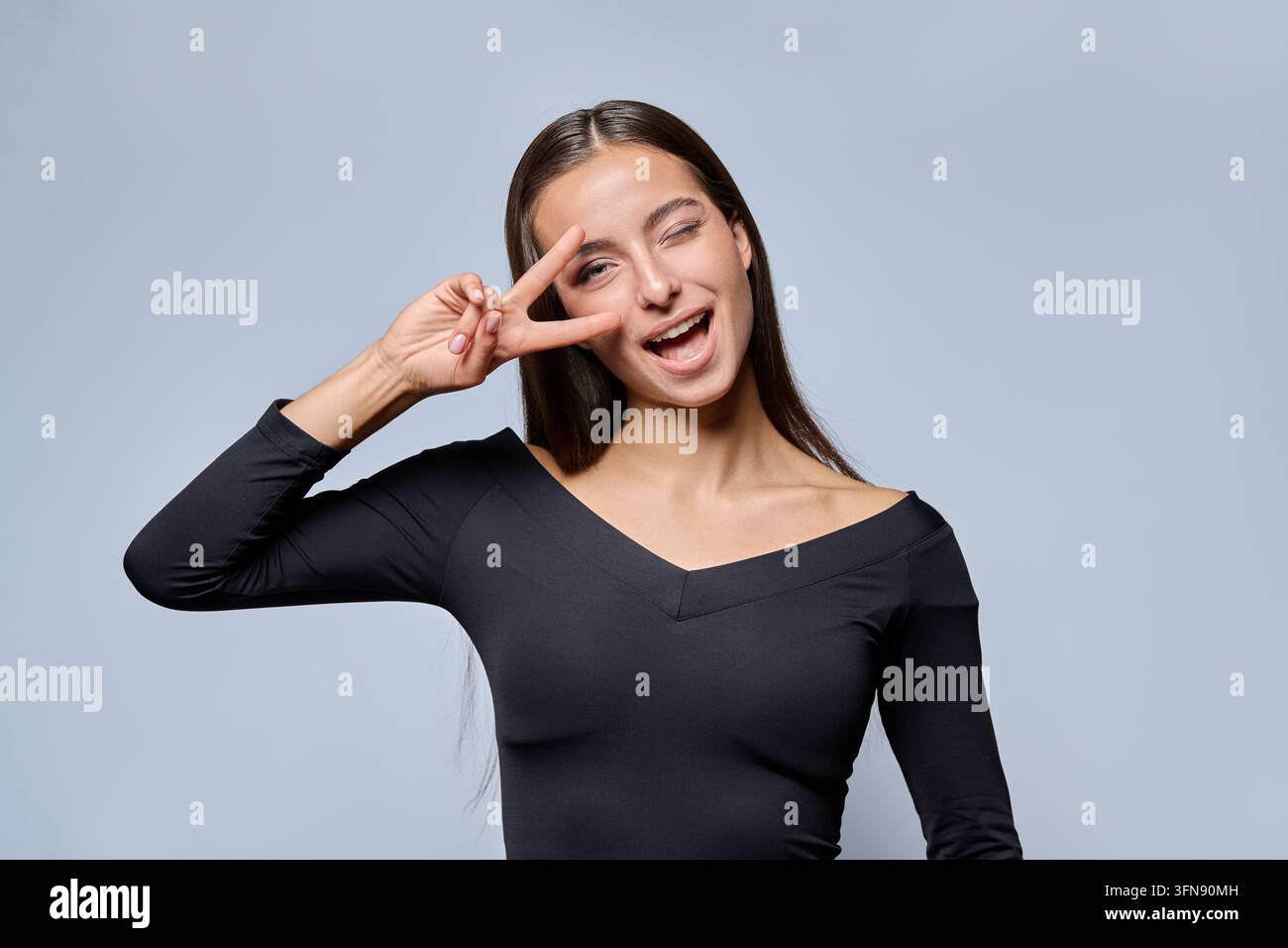 Giovane donna giocosa che mostra un segno di pace e ammicca su sfondo da studio Foto Stock