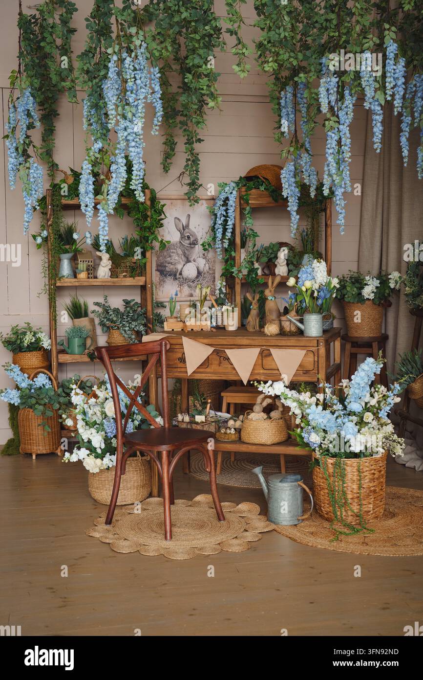 Elegante combinazione di legno naturale, tessuti e composizioni floreali. Fiori blu sospesi e accessori da giardino autentici creano un interno unico Foto Stock