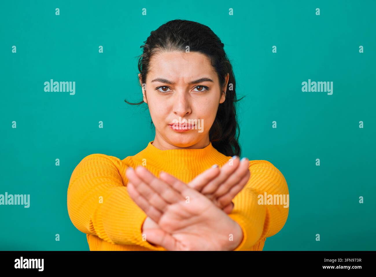 Giovane donna seria che fa un gesto di stop con le mani incrociate esprimendo rifiuto e confine Foto Stock