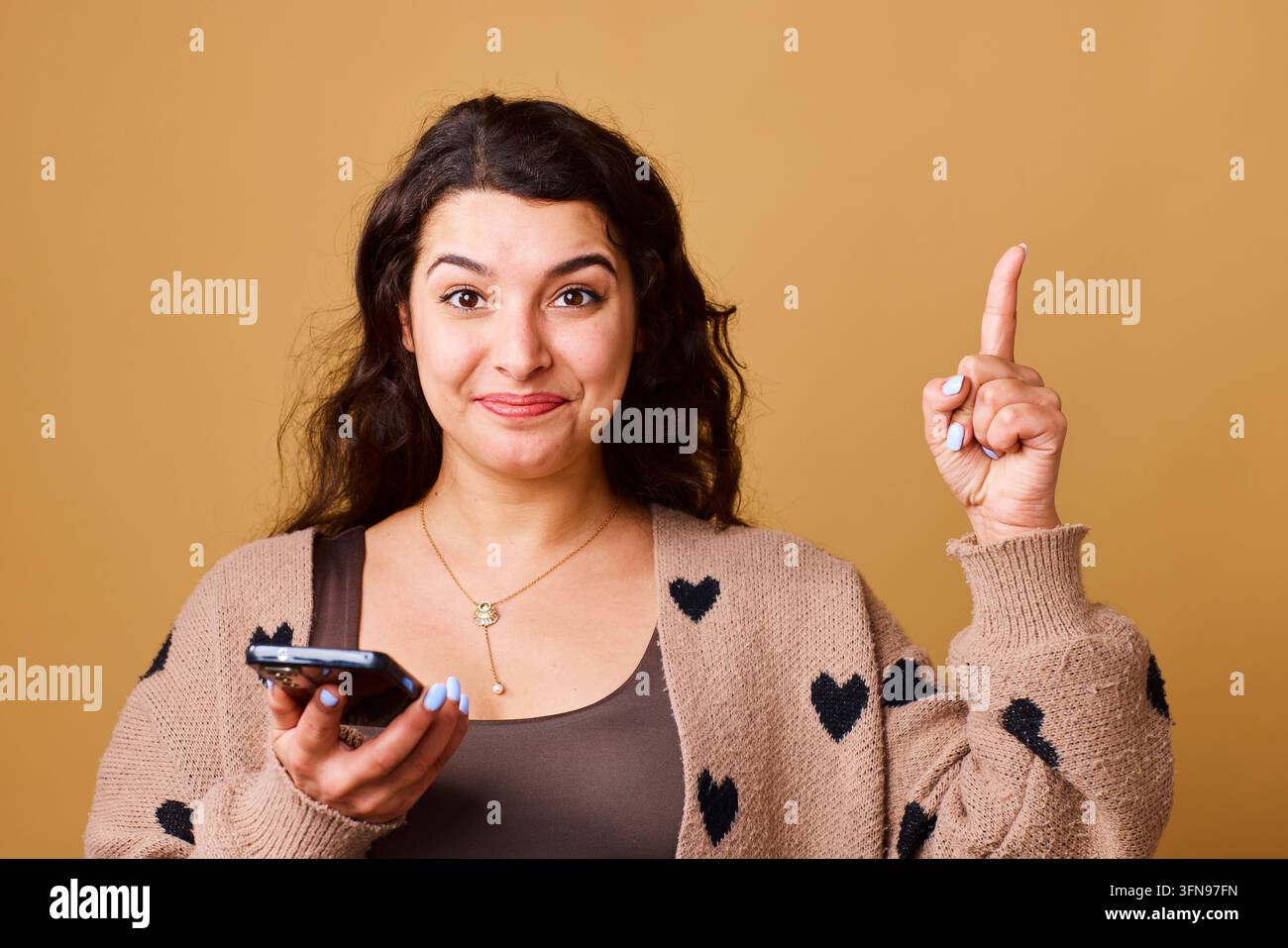 Donna sorridente che tiene uno smartphone puntato verso l'alto con un gesto di idea in un ritratto studio casual Foto Stock