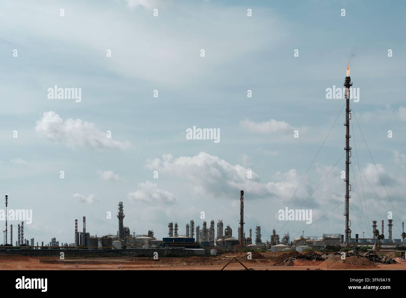 Alta pila di scarico industriale del gas con cavi di sostegno che bruciano gli idrocarburi in eccesso in una grande raffineria di petrolio greggio e un impianto di lavorazione petrochimica con fra Foto Stock
