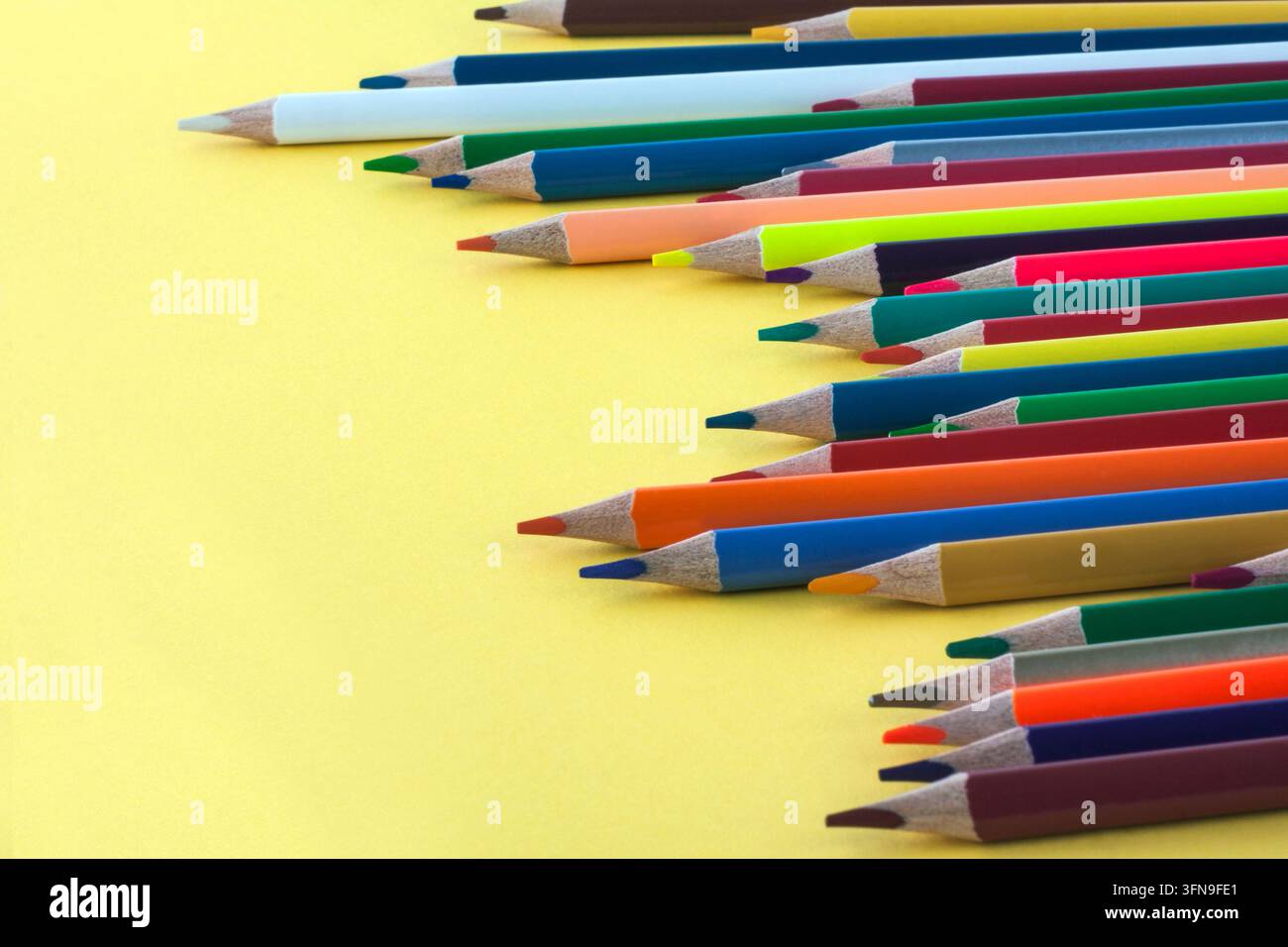 Pastelli colorati disposti su uno sfondo giallo brillante, creando una composizione vivace per l'arte, il disegno, la creatività, l'educazione e le forniture scolastiche Foto Stock