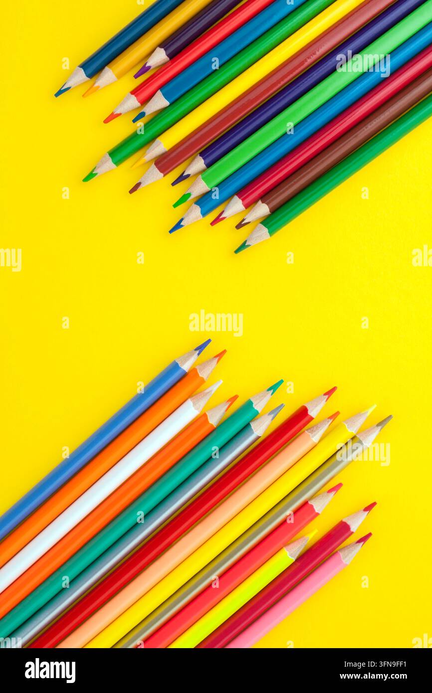Pastelli colorati disposti su uno sfondo giallo brillante, creando una composizione vivace per l'arte, il disegno, la creatività, l'educazione e le forniture scolastiche Foto Stock