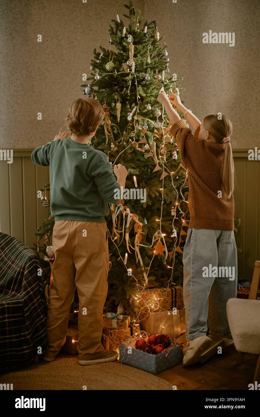 Bambini che decorano insieme l'albero di Natale a casa Foto Stock