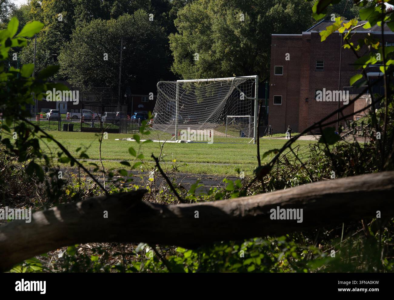 Un grande porta da calcio portatile con una rete cadente installata su un campo sportivo erboso incorniciato da alberi e un edificio in mattoni Foto Stock