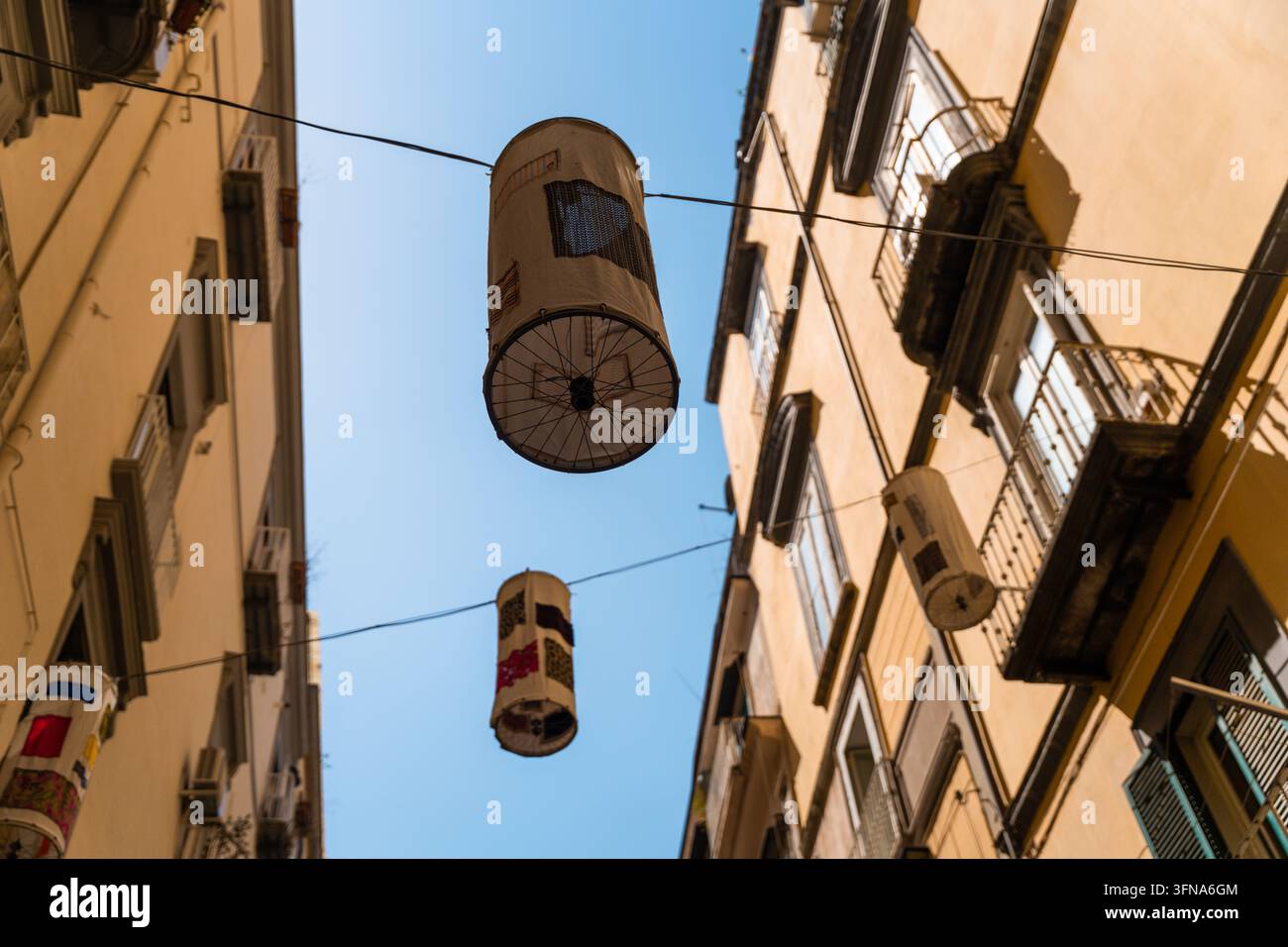 Vista di lanterne cilindriche decorative appese tra edifici storici gialli in una stretta strada a Napoli, Campania, Italia. Foto Stock