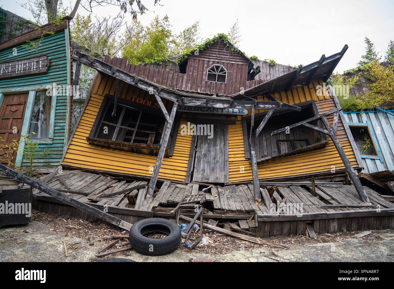 Vista di un edificio mercantile di legno cadente e inclinato con rivestimento giallo e tetto cadente in un'ambientazione rustica e abbandonata in Bulgaria. Foto Stock
