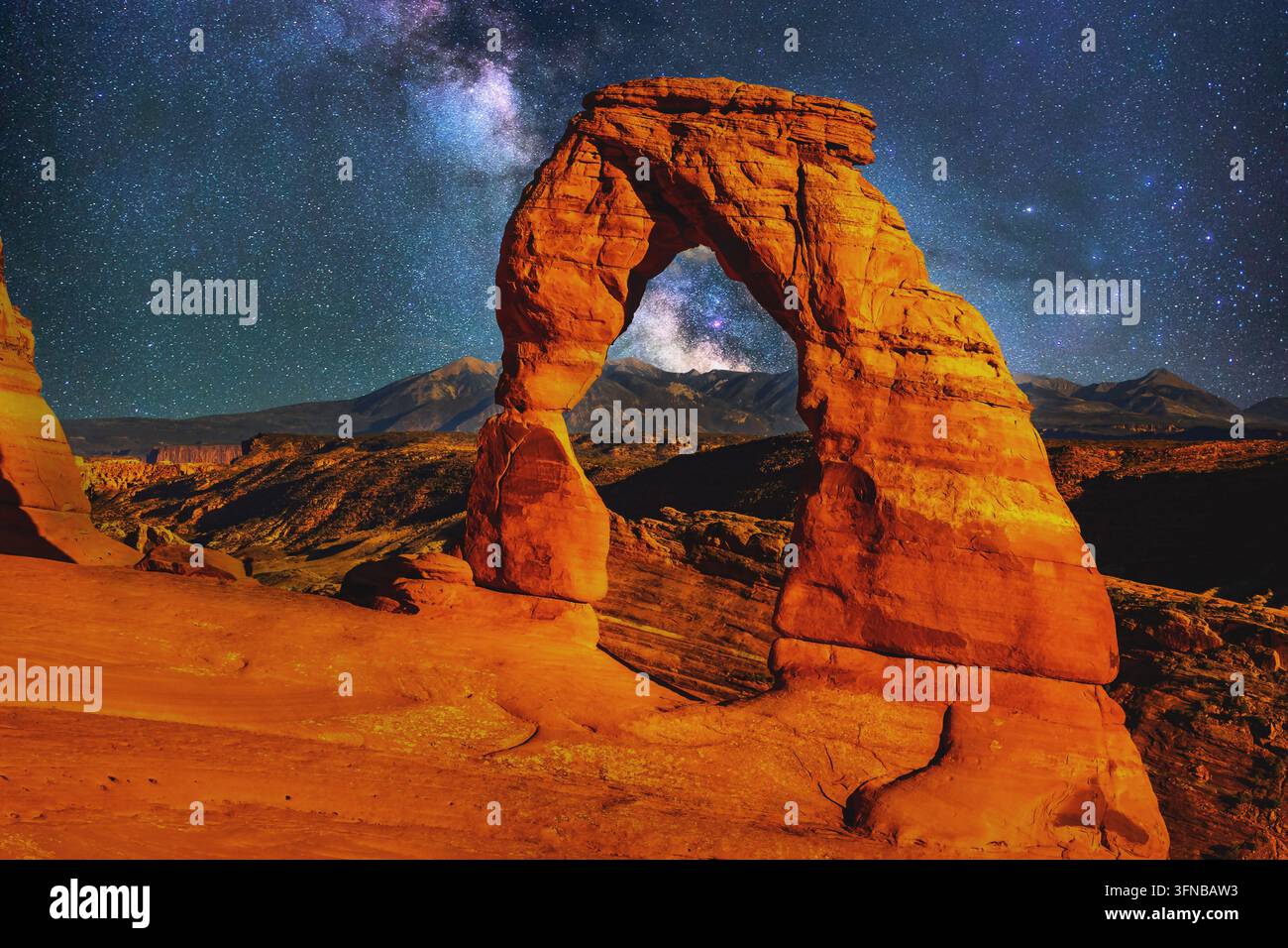 Un cielo notturno mozzafiato pieno di stelle della Via Lattea incornicia l'iconica Arco Delicato che si erge sopra il terreno roccioso rosso dell'Arches National Park nello Utah Foto Stock