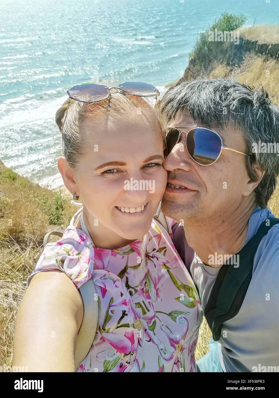 Coppia gioiosa che scatta una foto selfie su una scogliera sul mare con il Mar Nero sullo sfondo in Ucraina. Vacanze estive, stile di vita attivo e romanticismo - Immagine stock catturata con smartphone