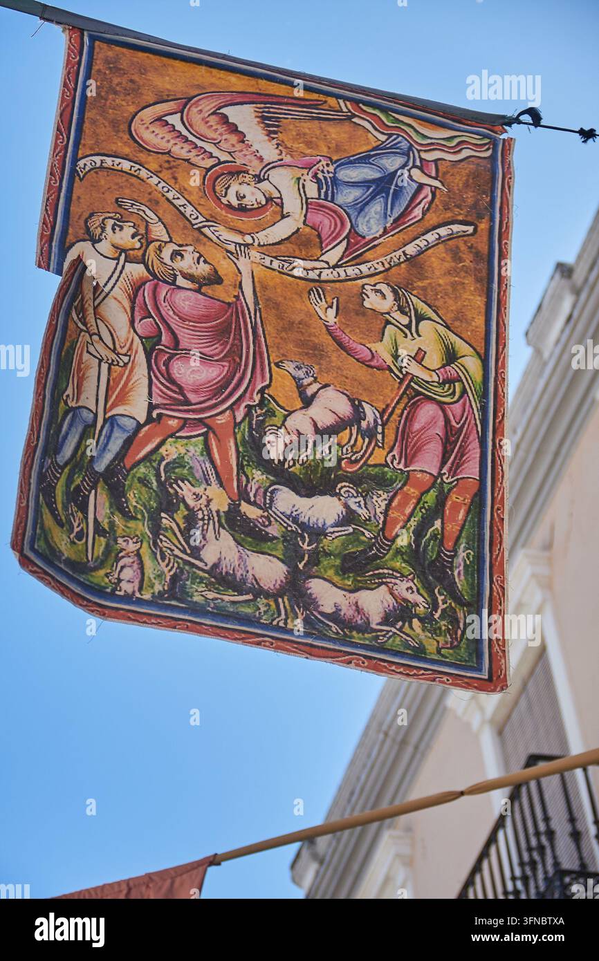 Stendardo religioso illustrato con un angelo, figure e pecore appeso sopra una strada durante il festival Capitulaciones de Santa Fe. Foto Stock