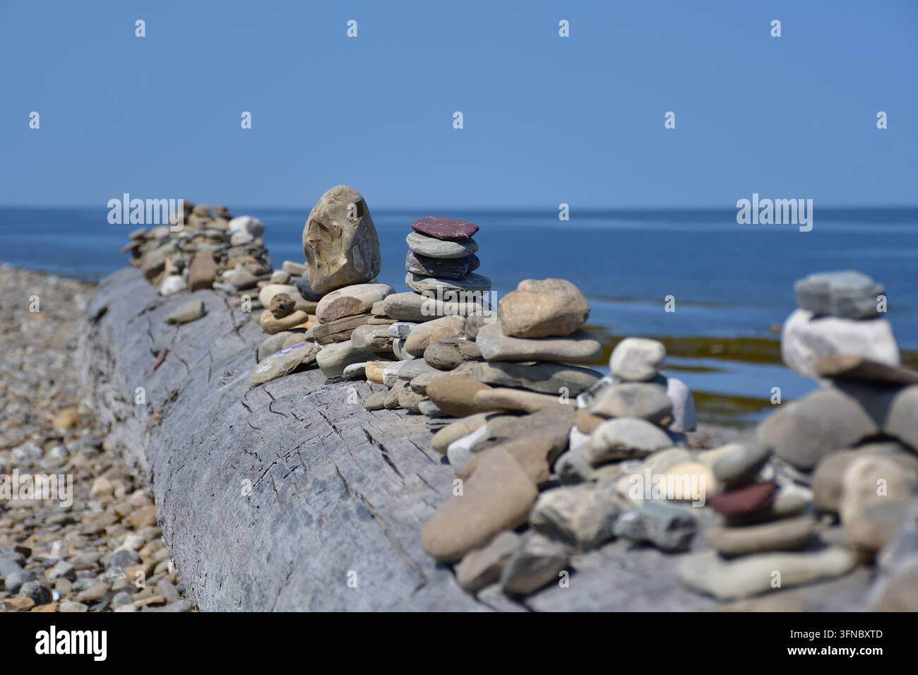 Busto di legno su spiaggia di ciottoli con inukshuk. Piccolo mucchio di pietre. Foto Stock