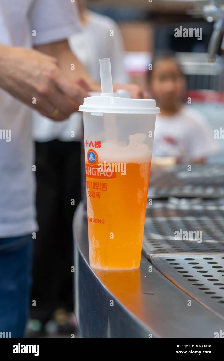Mano che versa birra fresca in un bicchiere di plastica con una cannuccia durante un evento Foto Stock