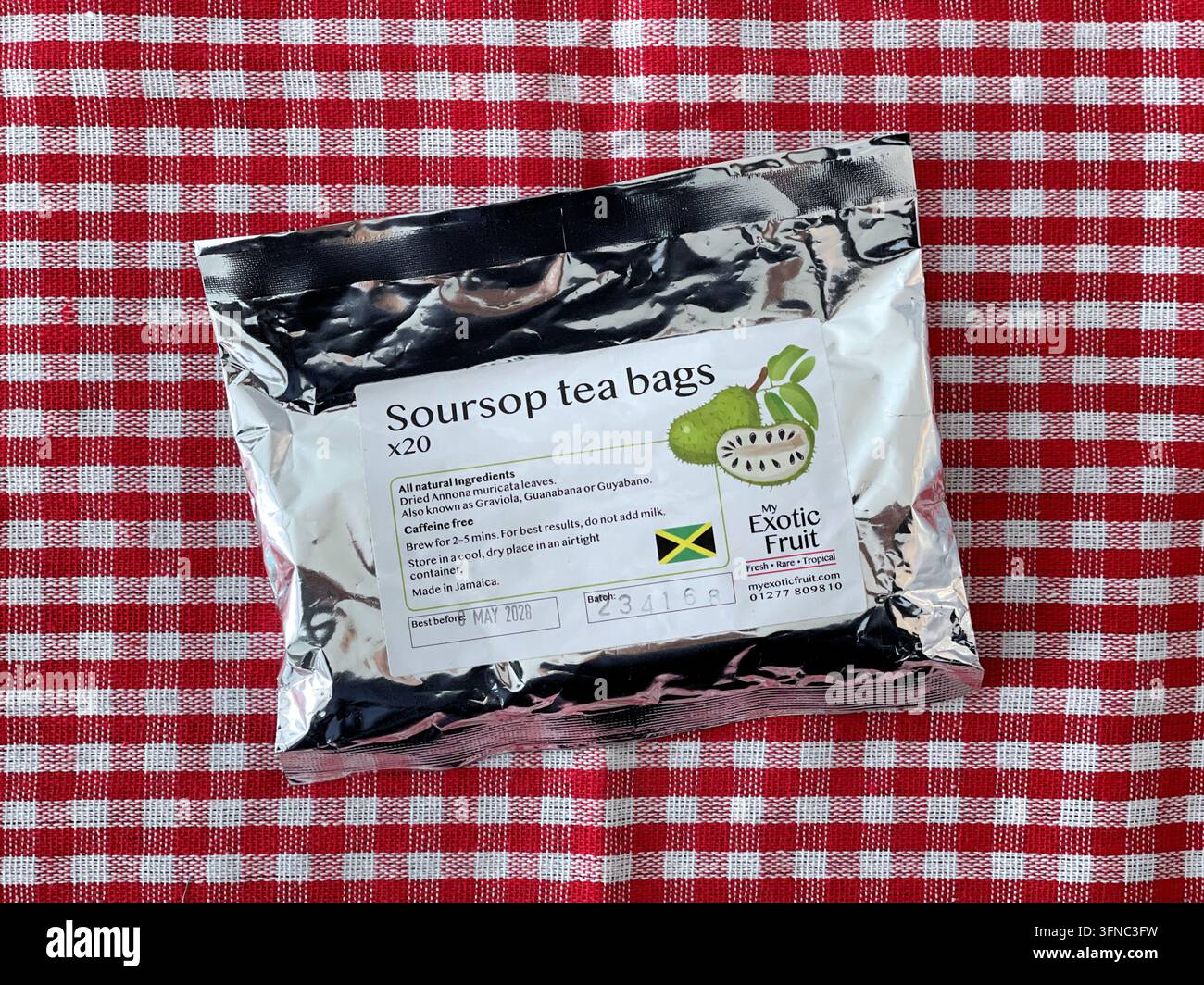 Una bustina di sacchetti di tè Soursop non aperta in una confezione di foglio su una tovaglia a quadri rossi, una bevanda rinfrescante con possibili benefici per la salute Foto Stock