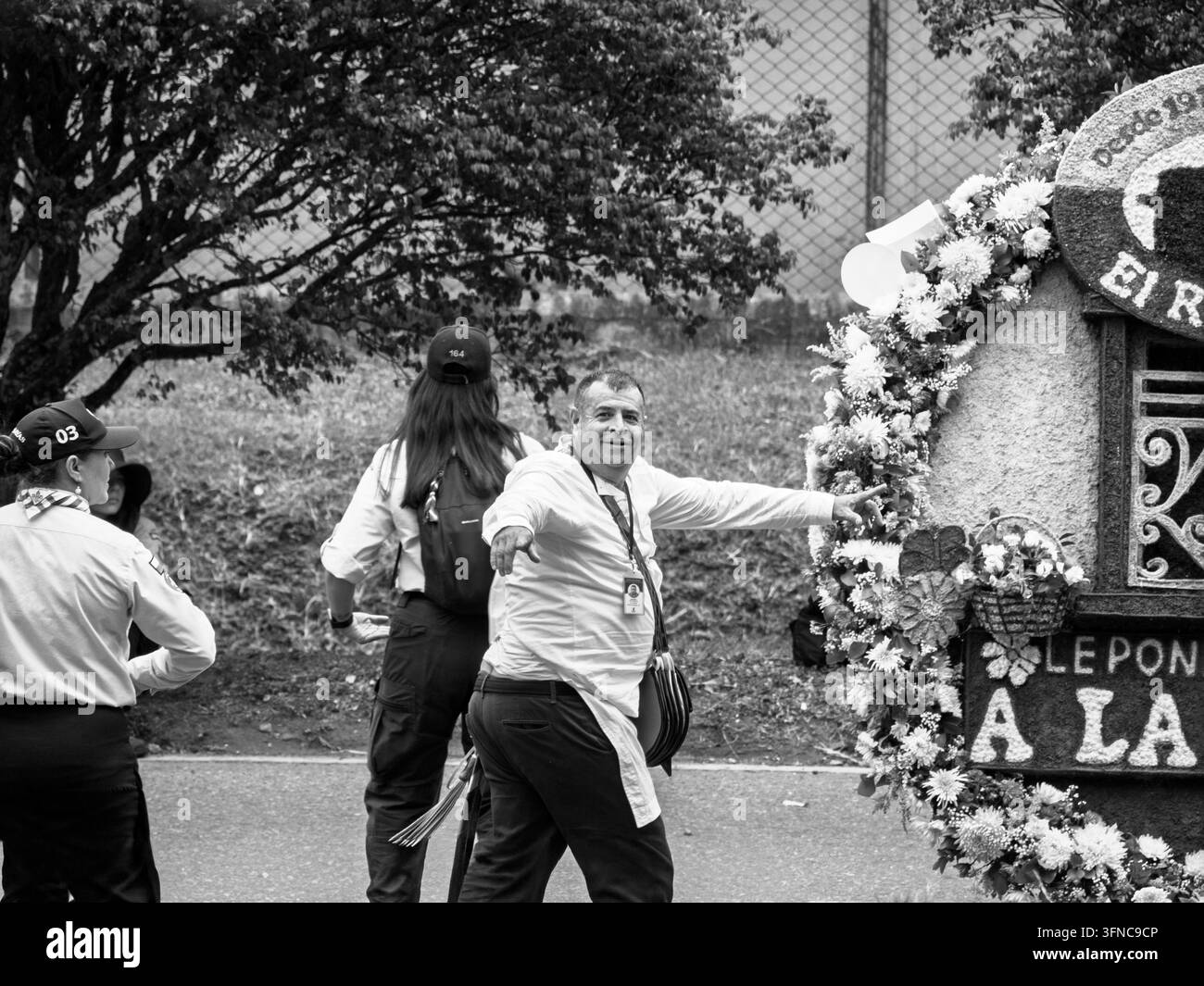 Fotografia in bianco e nero di un interprete maschile silletero sorridente, in piedi con le braccia aperte in segno di celebrazione accanto a una grande esposizione di fiori durante Foto Stock