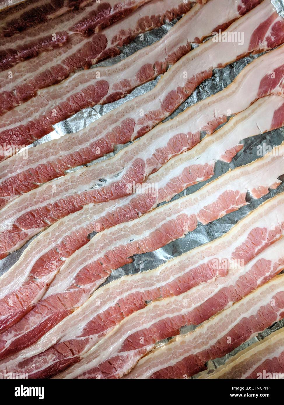 Una dozzina di strisce di pancetta cruda sono disposte su una teglia da forno in preparazione alla cottura. Foto Stock