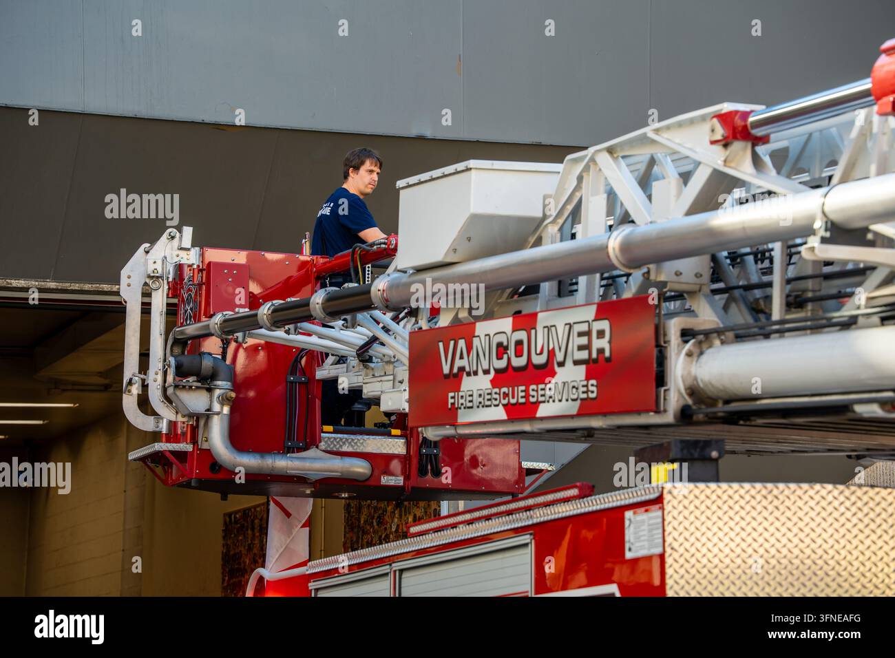 Un vigile del fuoco che controlla la piattaforma dell'ascensore aereo su un camion dei pompieri (autoscala) a Vancouver, British Columbia BC, Canada Foto Stock