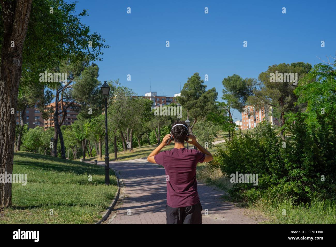 Fotografia da prospettiva posteriore di un giovane che cammina lungo un sentiero del parco ascoltando musica con le cuffie. Foto Stock