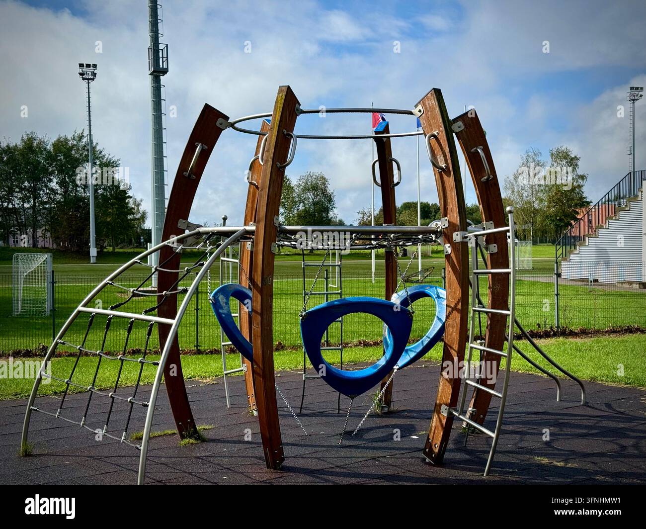 Struttura di arrampicata moderna per bambini in legno e metallo con altalene blu posizionata su una superficie di sicurezza in gomma in un parco sportivo all'aperto. - Immagine stock catturata con smartphone