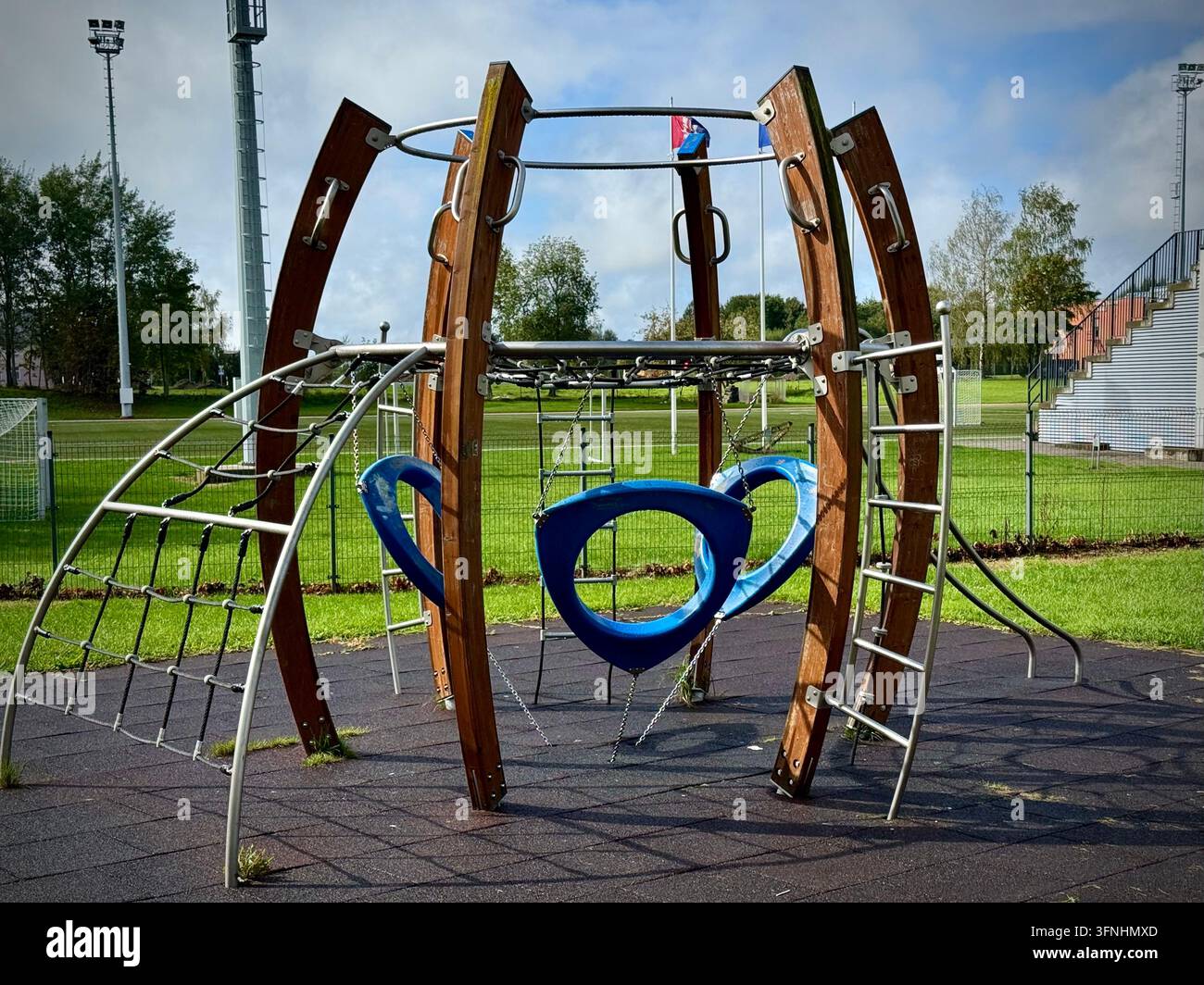 Struttura di arrampicata moderna per bambini in legno e metallo con altalene blu posizionata su una superficie di sicurezza in gomma in un parco sportivo all'aperto. - Immagine stock catturata con smartphone