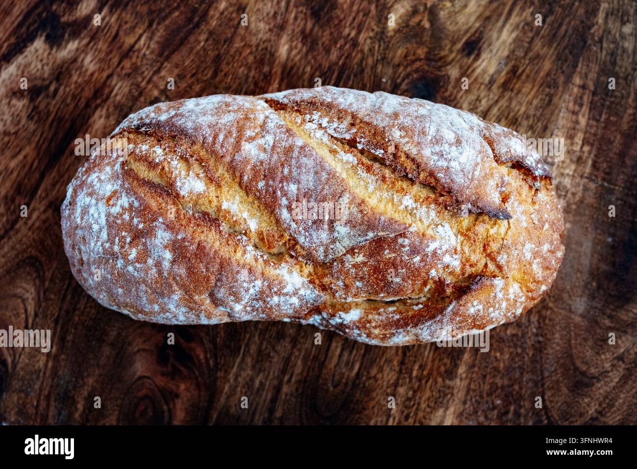 Panino rustico artigianale spolverato di farina su tavolo di legno scuro – vista dall'alto che mostra una crosta dorata incisa con texture di crepe Foto Stock