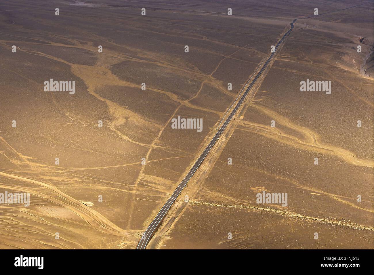 Vista aerea di un'autostrada rettilinea che attraversa un paesaggio desertico arido, con binari ramificati, modelli di erosione e toni caldi naturali della terra che creano un Foto Stock